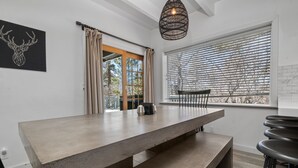 A modern kitchen with a large island, a dining area with a bench, and a view through the window.