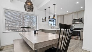 A modern kitchen with a large island, pendant lights, and a view through the window.