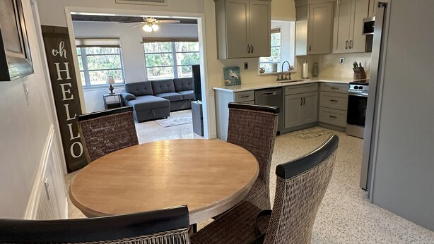 A modern kitchen with grey cabinets, a wooden dining table, wicker chairs, and a ceiling fan. - 2 Minutes to Downtown Crystal River, Large Fenced Yard, Boat Ramp, Pets OK ! (Crystal River)