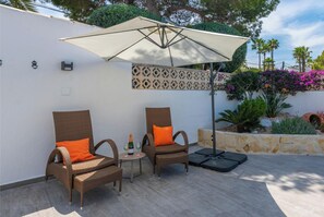 An outdoor seating area with two wicker chairs, a table with a bottle and glasses, and a large umbrella.