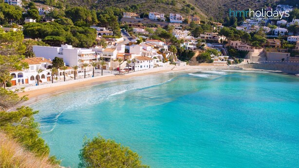 A coastal town with clear turquoise waters, white buildings, and a hillside in the background. - Bella Portet - cosy apartment in El Portet (Moraira)