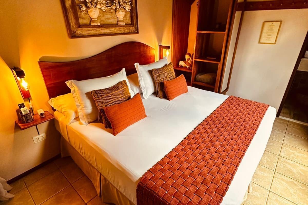 Ein Hotelzimmer mit einem großen Bett, einem Nachttisch mit Lampe, einem gerahmten Kunstwerk an der Wand und einem Holzschrank.