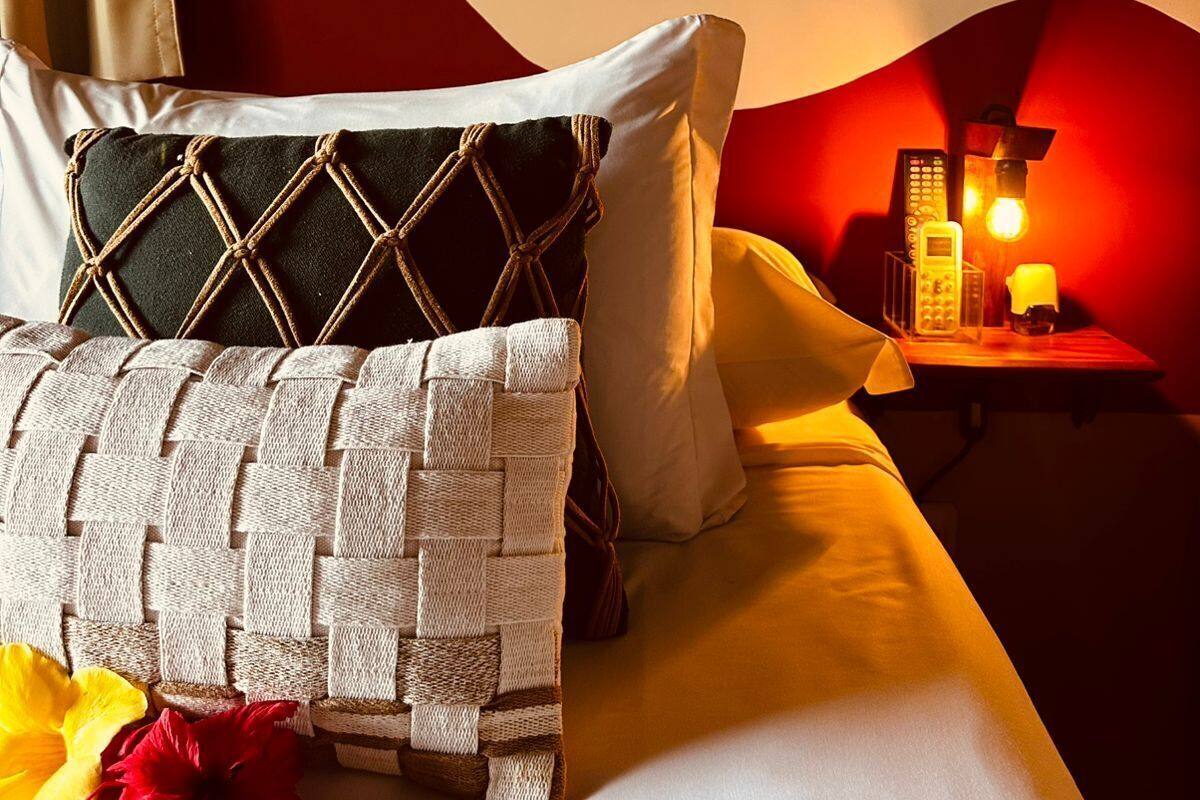 Ein Hotelzimmer mit Bett, Kissen, einem Nachttisch mit Lampe und einer Wand mit rotem Akzent.