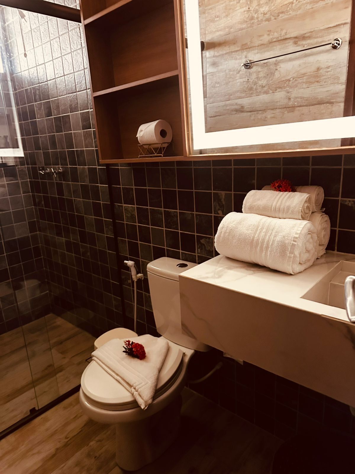 A bathroom with a toilet, a sink, a mirror, and a shelf with towels.