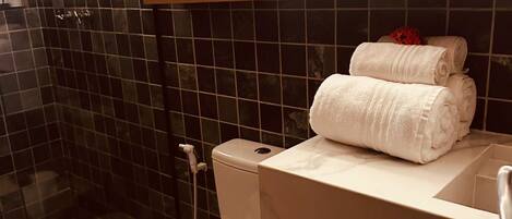 A bathroom with a toilet, a sink, a mirror, and a shelf with towels.
