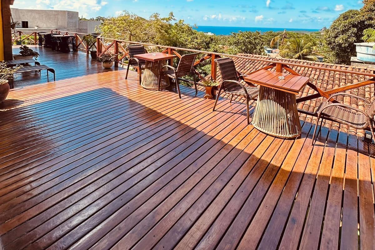 Eine Holzterrasse mit Gartenmöbeln, blauem Himmel und Blick auf den Ozean.