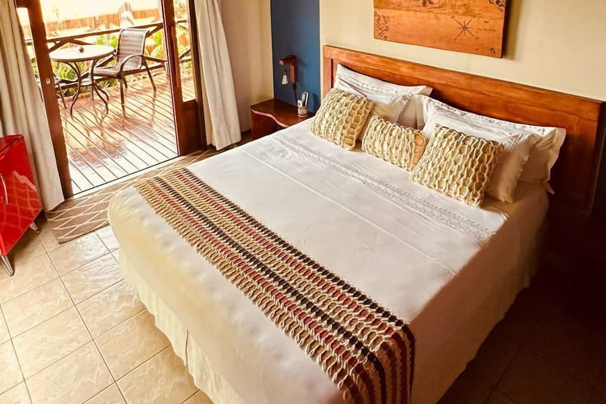 Ein Schlafzimmer mit einem großen Bett, einer Holzzahlende, einem Gemälde an der Wand und Blick ins Freie durch eine Schiebetür.