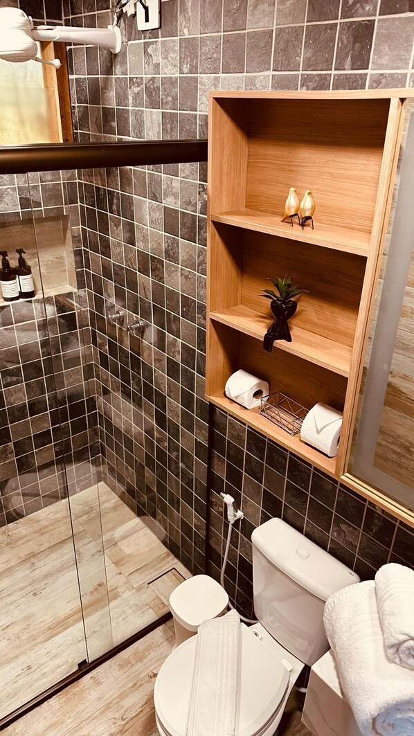 A modern bathroom with a shower, toilet, and wooden shelves with toiletries. - Pousada Pedras Secas (Fernando de Noronha)