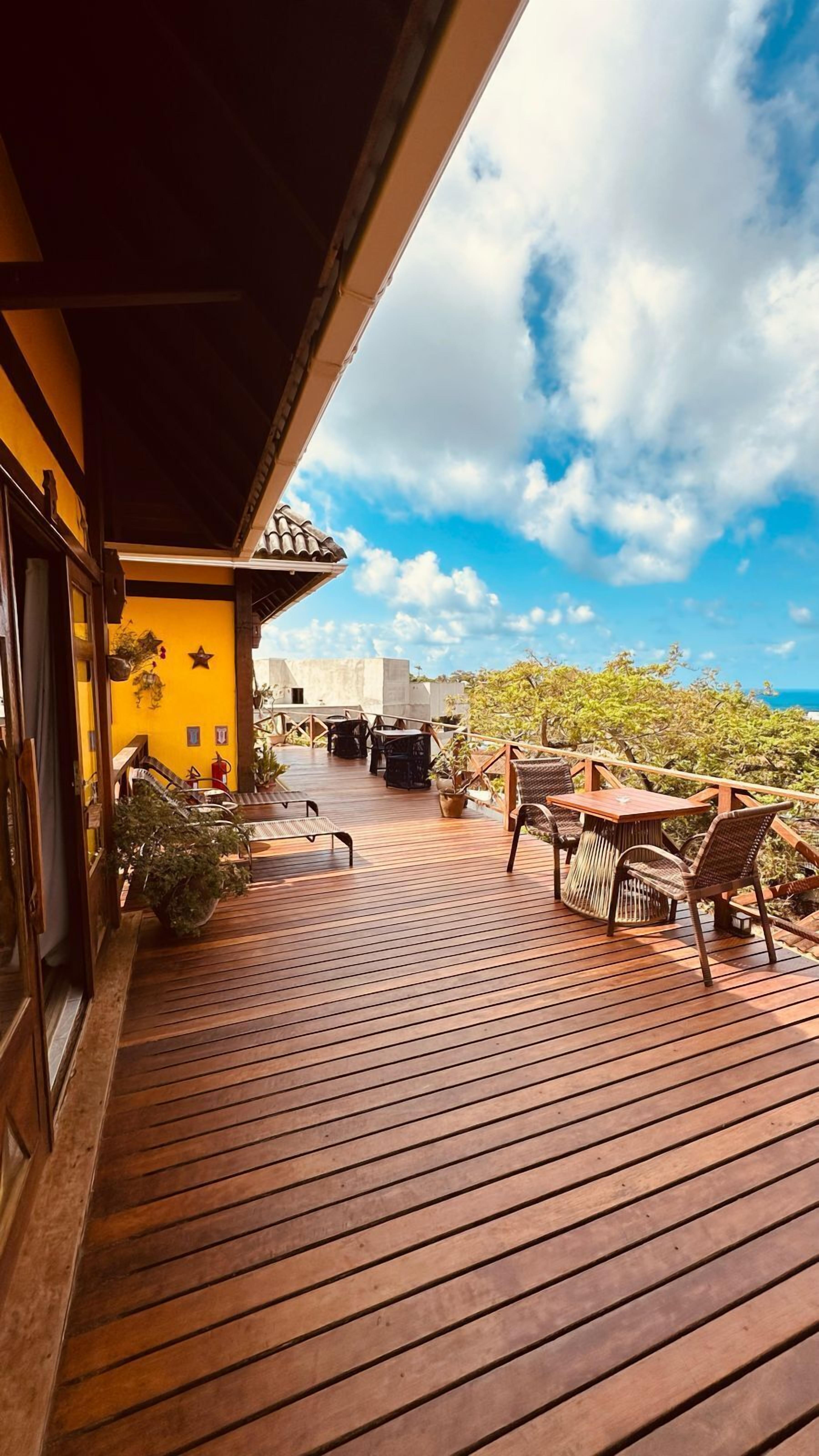 A wooden deck with outdoor furniture, a yellow wall with decorations, and a view of the sky and trees.