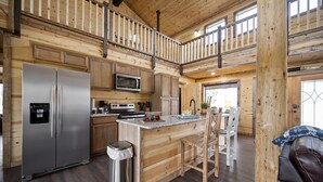 A spacious kitchen with a stainless steel refrigerator, microwave, and stove, wooden cabinetry, and a large island with seating. - Large River front cabin overlooking Glover River (Broken Bow)