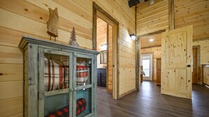 A wooden interior with a glass-fronted cabinet displaying plaid blankets, a wooden door, and a hallway leading to another room. - Large River front cabin overlooking Glover River (Broken Bow)