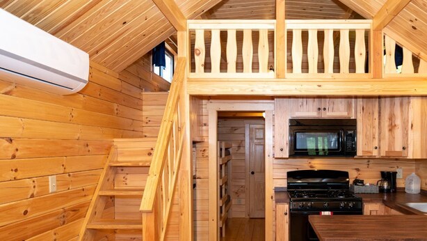 A wooden cabin interior with a kitchen area, wooden staircase, and a loft bedroom. - 126) Zonetail Log Cabin. Close to Hocking Hills State Park and more! (Logan)