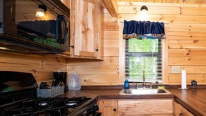 A wooden cabin kitchen with a stove, sink, and cabinets. - 126) Zonetail Log Cabin. Close to Hocking Hills State Park and more! (Logan)