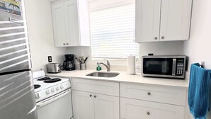 A compact kitchen with white cabinets, a stove, a microwave, and a coffee maker. - Southwinds #9 for 3, King Studio Steps to Beach (Hollywood)