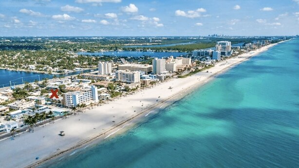 An aerial view of a coastal city with a long beach, clear blue waters, and a dense cluster of hotels and buildings along the shore. - Southwinds #9 for 3, King Studio Steps to Beach (Hollywood)