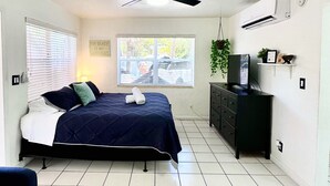 Una camera da letto con un letto, un ventilatore a soffitto, una finestra, una cassettiera e un condizionatore d'aria fissato al muro.