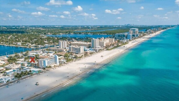 An aerial view of a coastal city with a long sandy beach, clear blue waters, and a mix of high-rise and low-rise buildings. - Hollywood Boardwalk Studio Fully Equipped Kitchen (Hollywood)