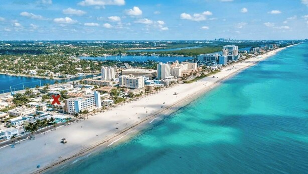 Luftaufnahme einer Küstenlandschaft mit Strand, Hotels und einem Yachthafen.