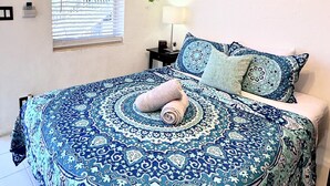 Ein Schlafzimmer mit einem gemusterten Bettüberwurf, einem zusammengerollten Handtuch und einer hängenden Pflanze.