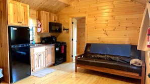 A compact cabin-style room with a kitchenette, a black refrigerator, a microwave, a stove, and a brown leather sofa.