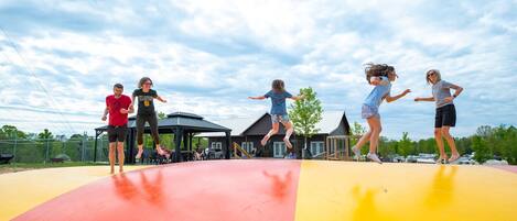 Eine Gruppe von Menschen springt draußen auf einer Trampolinanlage unter blauem Himmel.