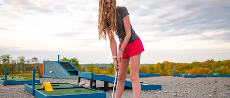 Una persona juga a mini-golf sobre un camp verd amb vores blaves i una pilota rosa.