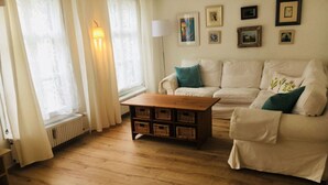A living room with a wooden floor, a white sofa, a wooden coffee table, and a radiator. - Stylish designer vacation apartment 2, 81sqm, WLAN, SAT, 1st floor (Monschau)