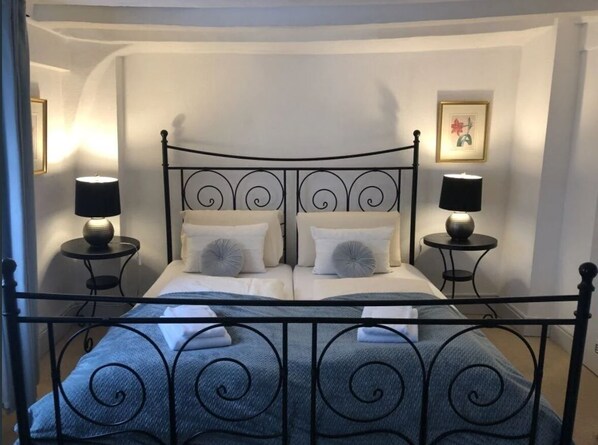 Un letto ben rifatto con testiera in metallo, due comodini con lampade e un quadro appeso al muro.