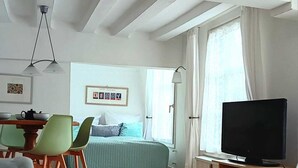A modern, well-lit room with a bed, a TV, a dining area with chairs, and a large window. - Stylish designer vacation apartment 2, 81sqm, WLAN, SAT, 1st floor (Monschau)