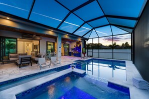 An indoor swimming pool with a glass ceiling, seating area, and a view of the sunset. - Costal Chic Vila w/Private Pool/Spa --5 min from the Beach! (Naples)