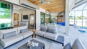 A modern living room with a sofa set, a coffee table, and a dining area with a kitchen in the background. - Costal Chic Vila w/Private Pool/Spa --5 min from the Beach! (Naples)
