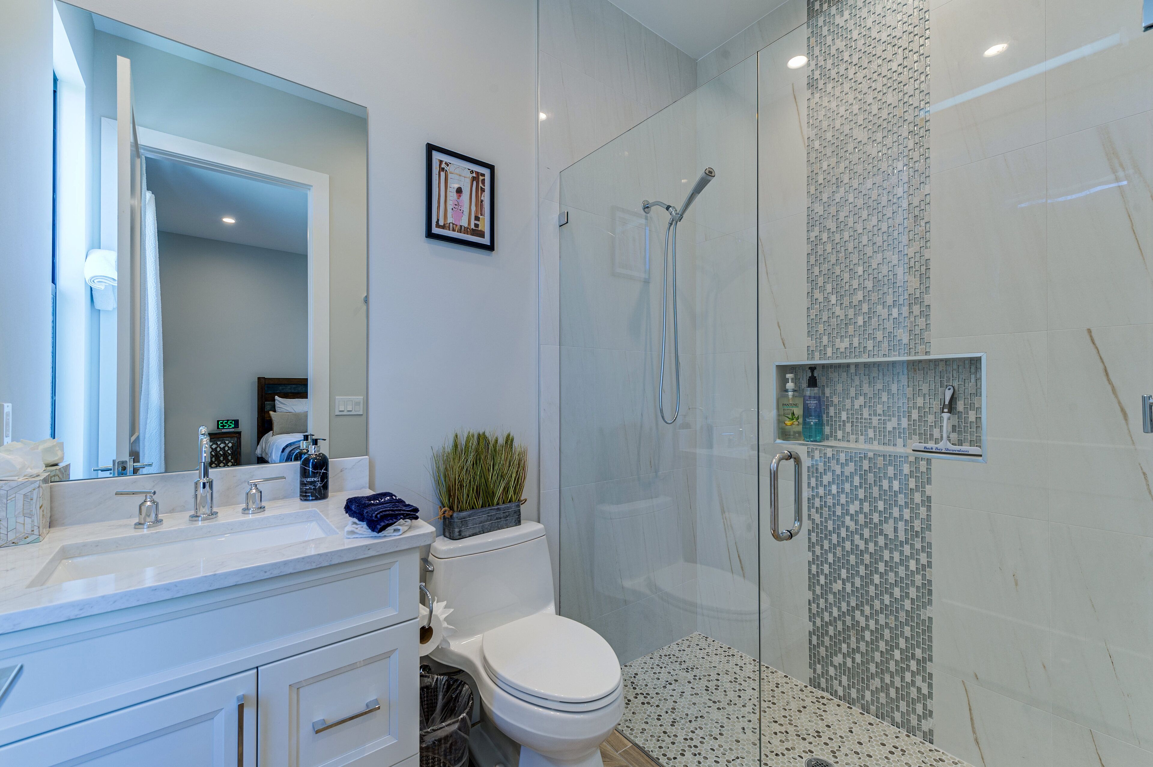 A modern bathroom with a glass-enclosed shower, a white sink with a mirror, and a toilet.