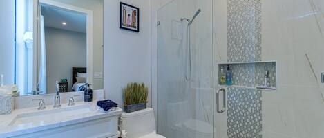 A modern bathroom with a glass-enclosed shower, a white sink with a mirror, and a toilet.
