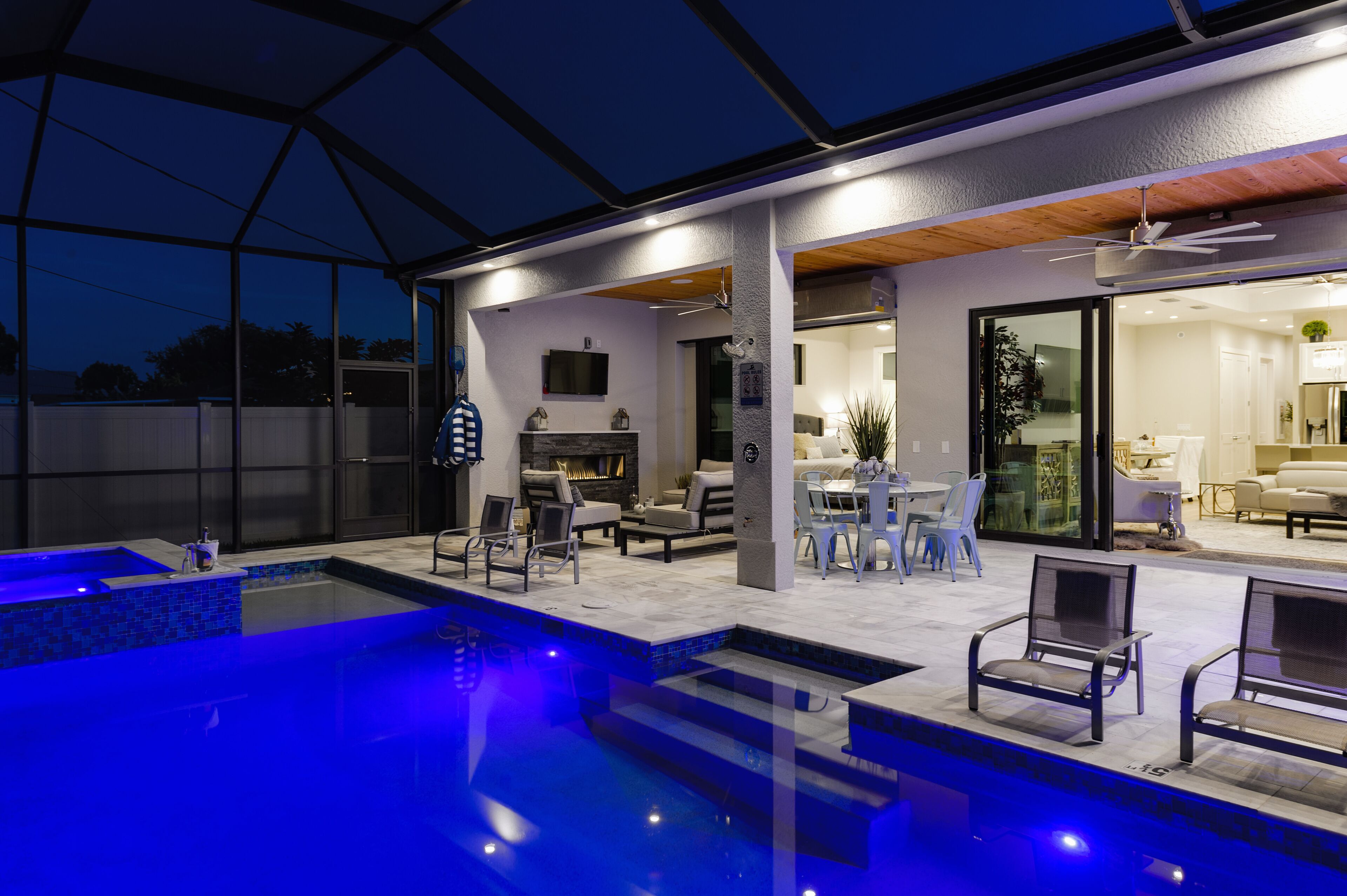 Ein moderner Poolbereich im Freien mit Glasveranda, Sitzgelegenheiten und Kamin.