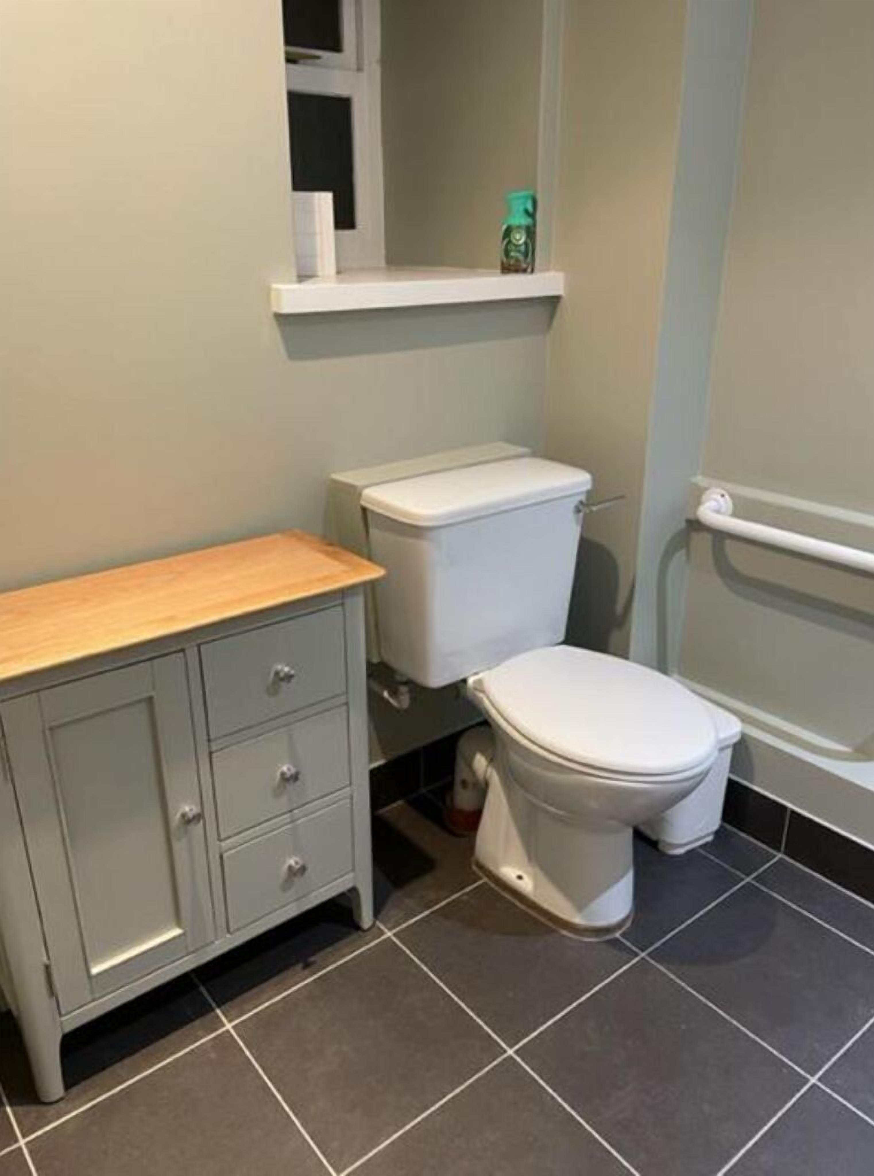 A bathroom with a toilet, a cabinet, and a shelf above the toilet.