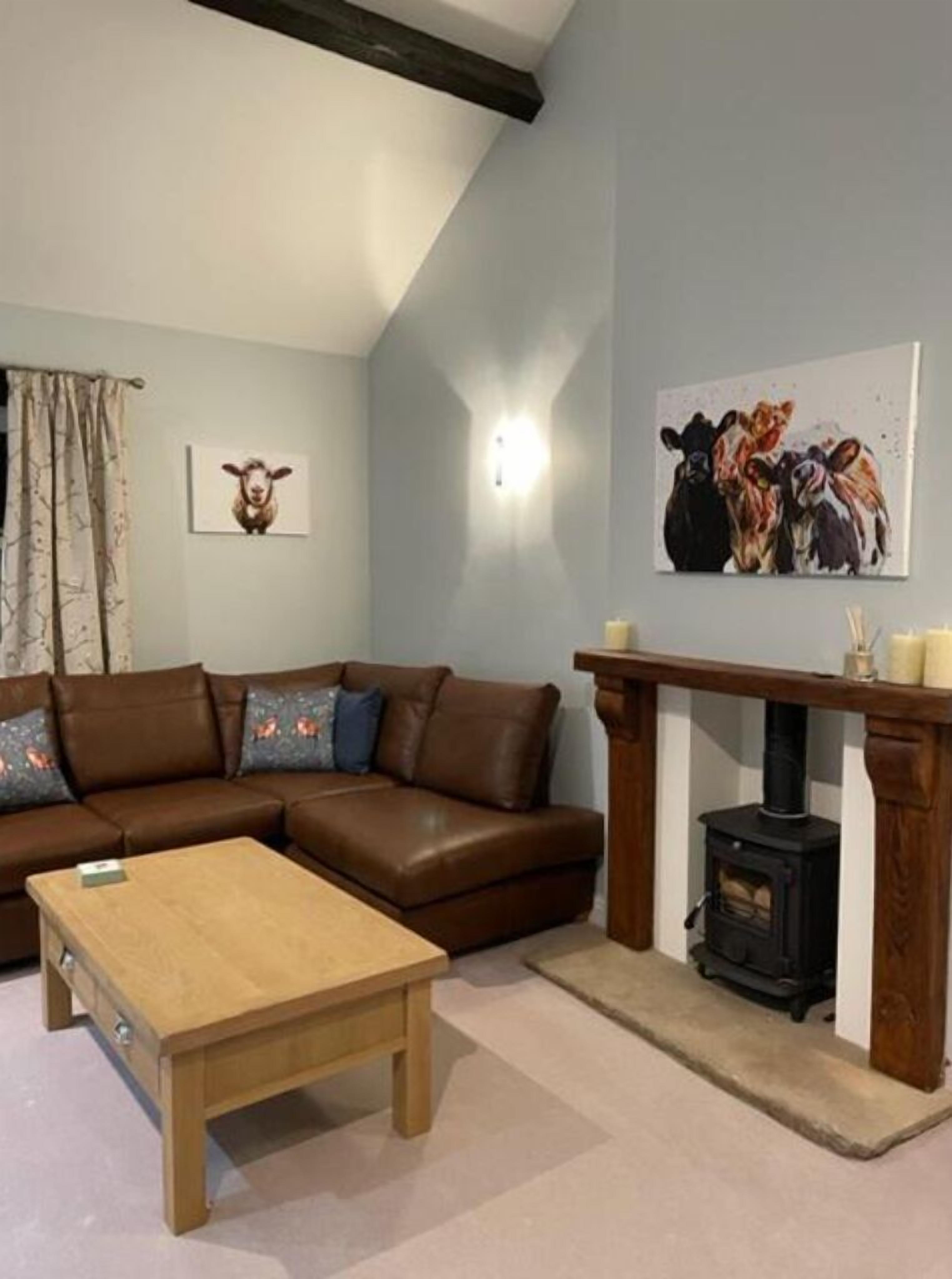 Een woonkamer met een bruine leren bank, een houten salontafel, een open haard en kunstwerken van koeien.