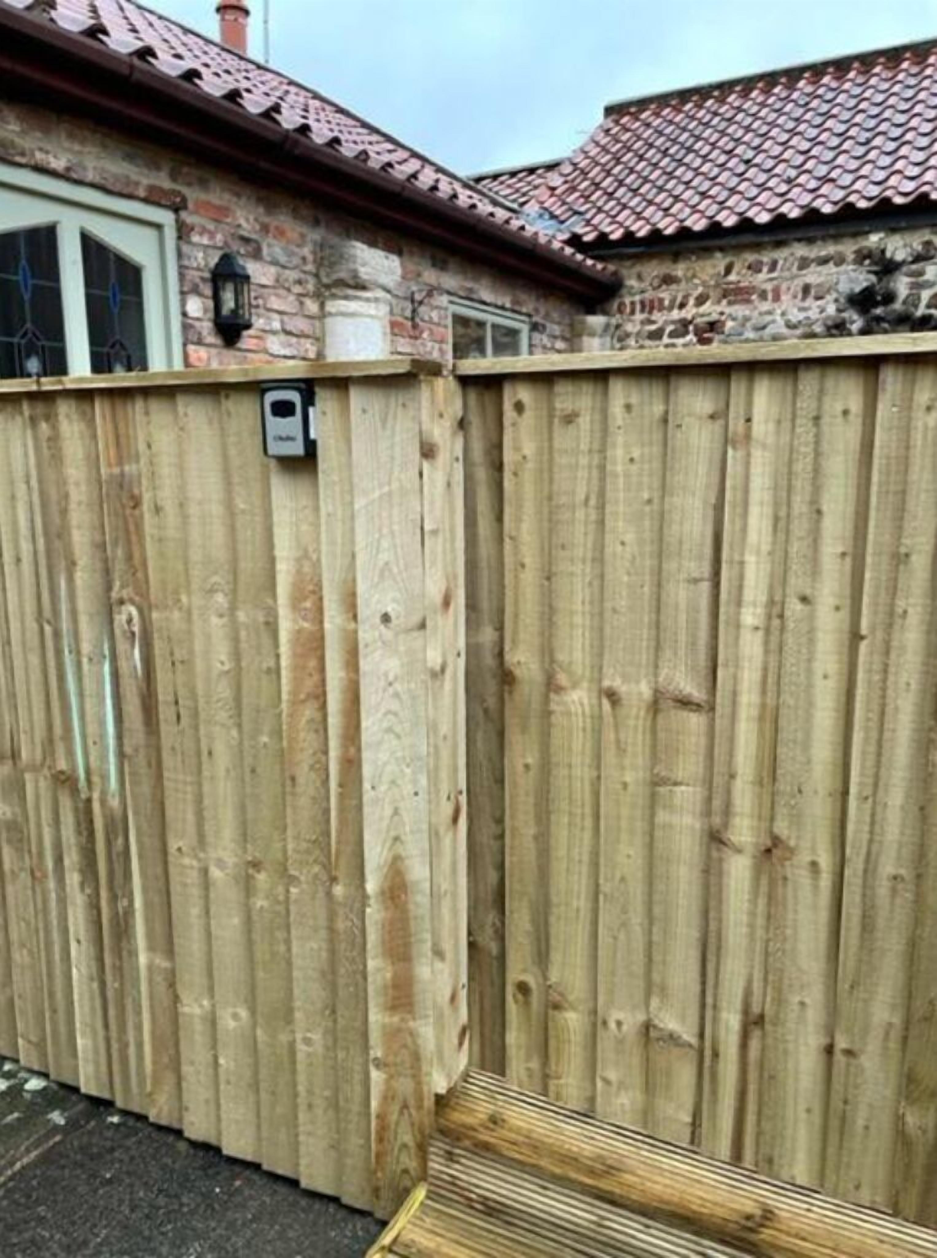A wooden fence with a small step leading up to a house with a tiled roof and a brick wall.