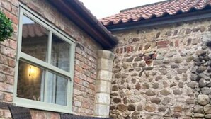 A stone building with a tiled roof and a window. There are wicker chairs and a table outside.