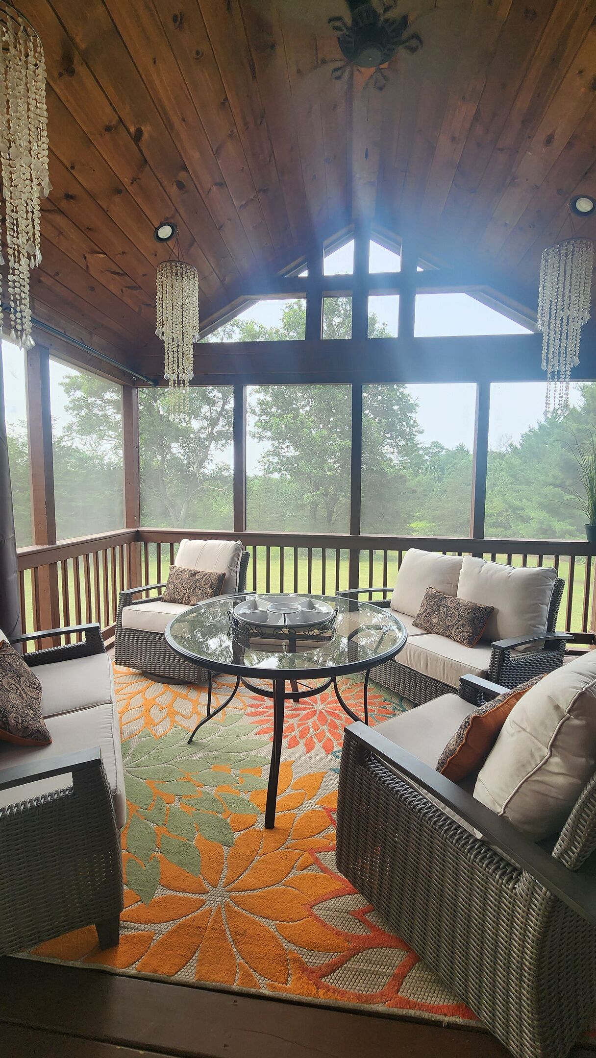 A covered patio with wicker furniture, a glass table, and a patterned rug.