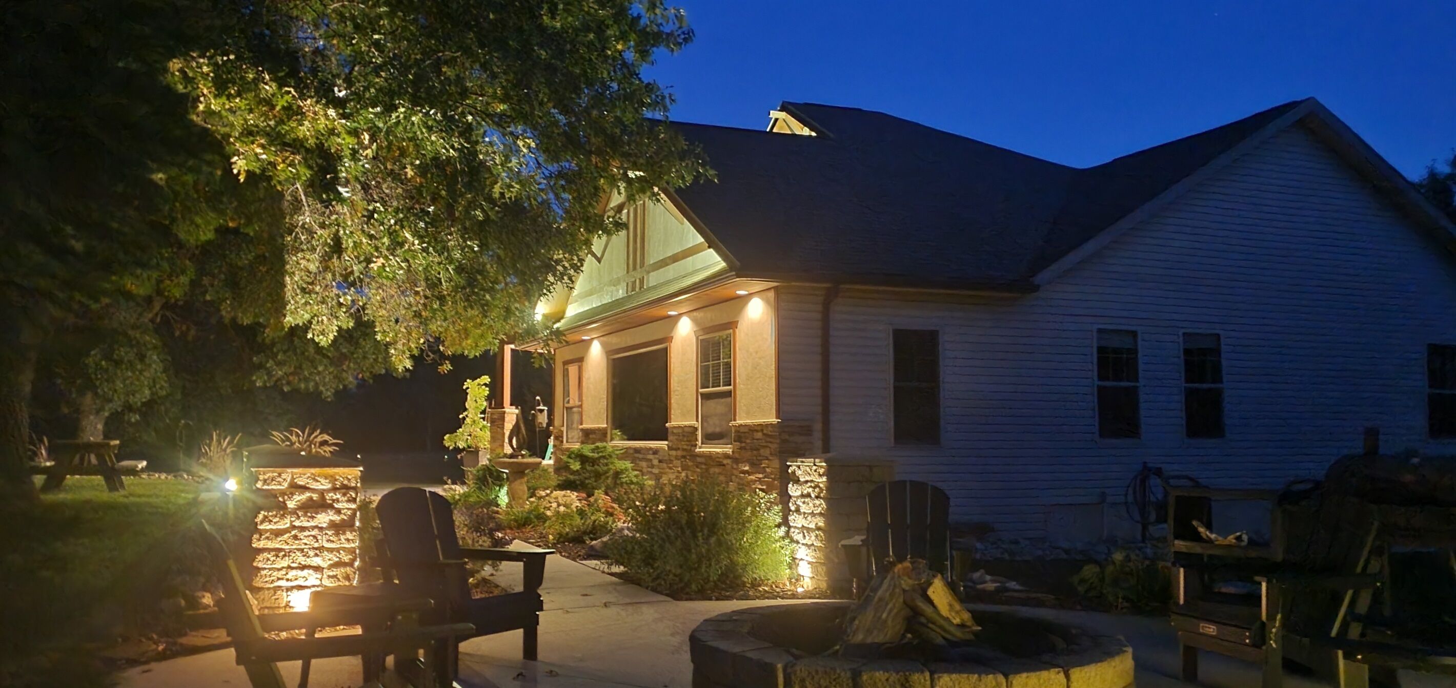 A house with a stone fireplace, outdoor seating, and a well-lit porch.