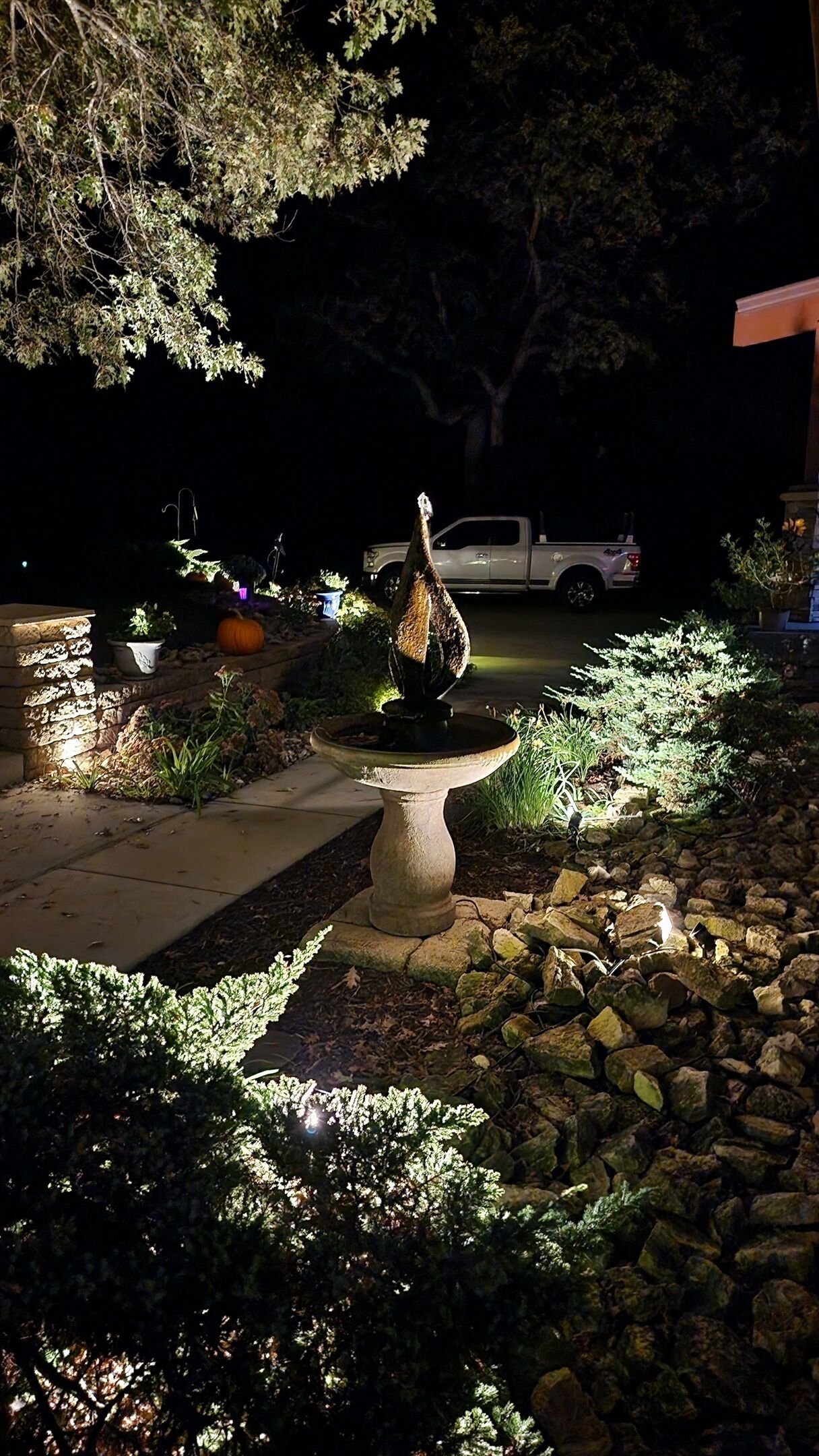 A garden with a birdbath, a white pickup truck, and a stone wall.