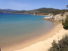A beach with clear water, sandy shore, and hills in the background.