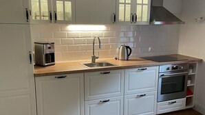 Eine kompakte Küche mit weißen Schränken, einem Edelstahlbackofen, einer Kaffeemaschine und einem Wasserkocher.