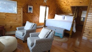A cozy log cabin bedroom with a four-poster bed, two patterned armchairs, a round ottoman, and a wooden floor. - Have an unforgettable getaway at a family sized beach house with private beach! (Steuben)