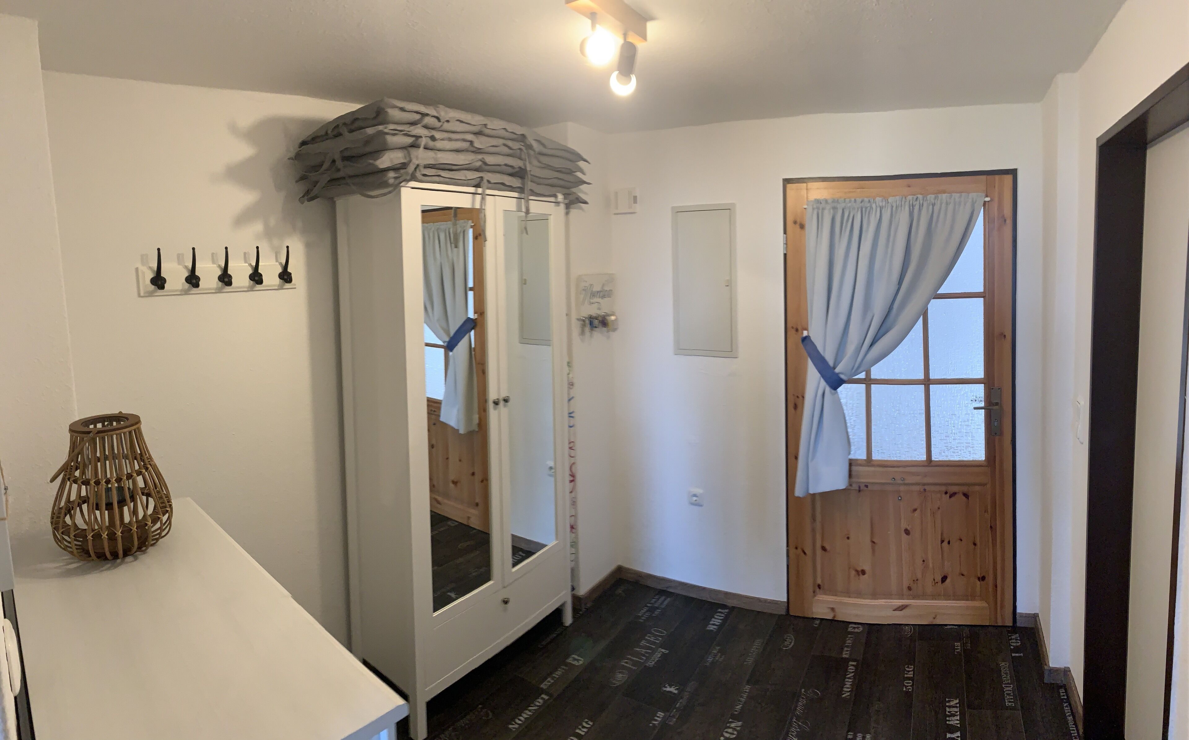 Une pièce avec une armoire blanche, un miroir, une porte en bois avec un rideau et un petit panier en osier.