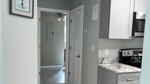 A kitchen with grey cabinets, a microwave, and a stove. There is a patterned rug on the floor and a framed picture on the wall.