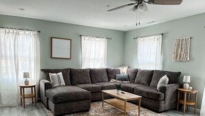 A living room with a sectional sofa, a coffee table, two side tables, a ceiling fan, and a patterned rug.