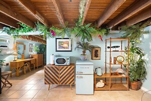Una habitación con techo de madera, un refrigerador blanco, una estantería de bambú y varias plantas.