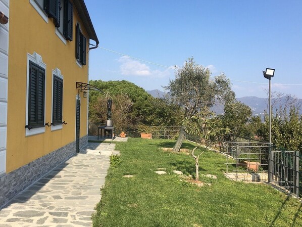 A yellow building with a stone pathway leading to a grassy area with a metal fence and a tree.