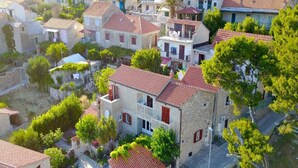 A traditional stone building with a red-tiled roof, surrounded by greenery and other residential structures. - Apartment Račić (Bol)